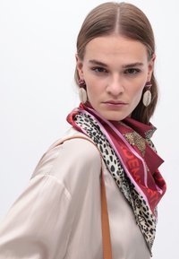 Silk scarf med livfulla röda, rosa och djurmönstrade nyanser, draperad runt halsen. Slät textur med en blandning av mönster och logotyp.