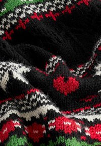 Strikket sweaterstof med mønstre i sort, rød, hvid og grøn, med hjerte-motiver og teksturerede sting, der fremhæver et hyggeligt design.