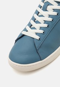 Kék bőr sneaker fehér fűzőkkel, sima textúrával, kerek orral és kontrasztos varrással a felső részen és a talpon.