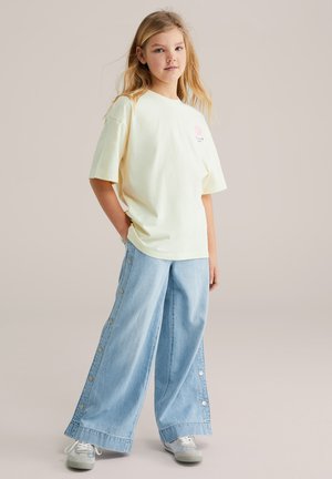 Camiseta de algodón amarilla con mangas cortas y estampado floral en rosa. Pantalones vaqueros de pierna ancha en azul claro con botones laterales y dobladillo sin rematar.