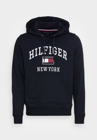 Sudadera azul marino hecha de tela suave, con un bolsillo frontal, capucha con cordones y un gran texto blanco "HILFIGER NEW YORK" con un logo.
