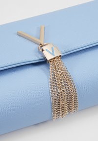 Ljusblå texturerad clutch med en guldkedjehänge och en metallisk "V"-detalj, med en slank rektangulär form och ett magnetiskt stängningssystem.