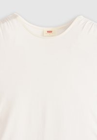 Camiseta blanca de manga corta con cuello redondo, hecha de un material de algodón suave y con un ajuste relajado. Etiqueta visible en el área del cuello.