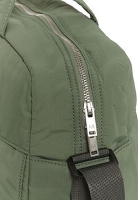 Približan posnetek zelene tkanine vrečke s srebrnim zadrgo in črnim nastavljivim trakom s plastično zaponko.