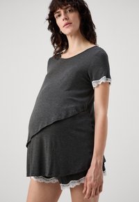 Sötét szürke anyagú kismama felső rövid ujjal. Fehér csipke díszítéssel a sleeveken és az alján. Kényelmes terhesség alatti viseletre tervezve.