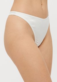 Perizoma bianco in satin con superficie liscia, spalline sottili e delicate bordature scallopate, che mette in risalto un design minimalista e una silhouette slanciata.