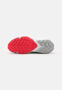 Semelle de chaussure de sport avec une bande de roulement rouge à l'avant et une bande de roulement grise avec des accents jaunes au talon sur fond blanc.