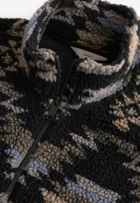 Czarna, brązowa i niebieska polarowa kurtka w wzory, z wysokim kołnierzem, półzamkiem z przodu i teksturowanym materiałem. Widoczna metka marki wewnątrz.