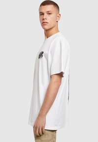 Hvid bomulds t-shirt med korte ærmer, prydet med sort tekstdesign på forsiden. Lige pasform og blød tekstur, vist i en sidevinkel.