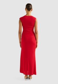Red, fitted maxi dress with cap sleeves, gathered detail at the waist, and a floor-length hem, paired with strappy gold heels.