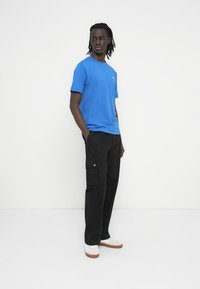 Μπλε βαμβακερό μπλουζάκι με κοντά μανίκια και στρογγυλή λαιμόκοψη, συνδυασμένο με μαύρο παντελόνι cargo με πλαϊνές τσέπες και ασημένιες λεπτομέρειες.