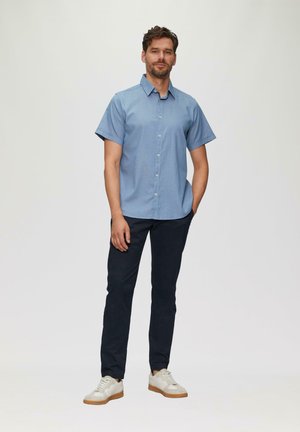 Lichtblauhem korte mouwen overhemd met knopen, donkere marineblauwe broek en witte sneakers met tan kleurige zolen; eenvoudig ontwerp met een kraag.