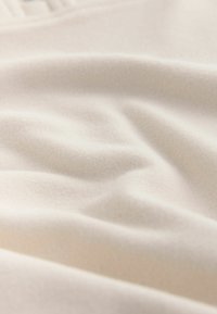 Mehka, kremno obarvana tkanina z gladko teksturo in nežnimi gubami, ki ima subtilne prehode barv in lahkoten videz.