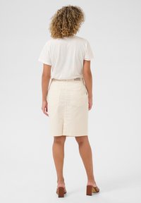 Crème-kleurige denim rok met opgestikte zakken, een rechte pasvorm en een split aan de achterkant. Gecombineerd met een wit t-shirt en bruine sandalen met blokhak.