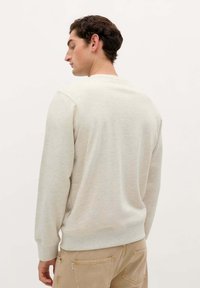 Sudadera gris claro hecha de tejido suave, con mangas largas y un cuello redondeado. Cuenta con un dobladillo y puños acanalados.