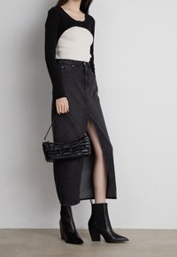 Top de manga larga negro y crema, falda de mezclilla negra de cintura alta con abertura lateral, botines negros de tacón y un bolso negro texturizado.