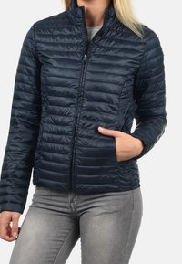 Granatowa kurtka puchowa z poziomym pikowaniem, wysokim kołnierzem, zapięciem na zamek oraz bocznymi kieszeniami. Lekka i gładka w dotyku.