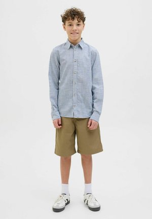 Chemise à manches longues à rayures bleues et blanches, associée à un short kaki, des chaussettes blanches et des baskets noires et blanches.