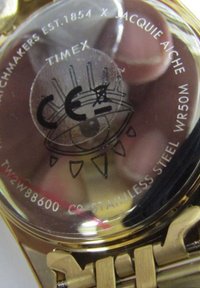 Rückseite der Uhr aus goldfarbenem Edelstahl mit eingraviertem Text, Wasserdichtigkeitsanzeiger und kreisförmigem Design mit einem stilisierten Auge.