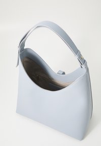 Sac à épaule en cuir bleu clair avec une silhouette arrondie, une texture douce et une seule sangle réglable. L'intérieur comporte une poche zippée.