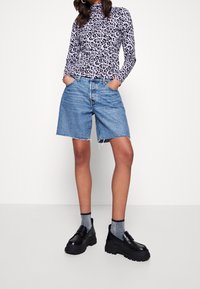 Długi rękaw, purpurowa bluzka w wzór panterki. Dżinsowe szorty z postrzępionym dołem. Czarny platformy z srebrnymi skarpetkami. Jednolity kolor tła.