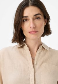 Light beige linen shirt featuring a button-up front, a soft texture, a chest pocket, and a classic collar. Simple, understated design.