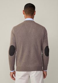 Ruskea neulottu villapaita mustilla kyynärpäätuilla, pyöreällä pääntiellä ja ribbausviittauksilla, kerrostettuna vaaleansinisen kauluspaitan päällä.