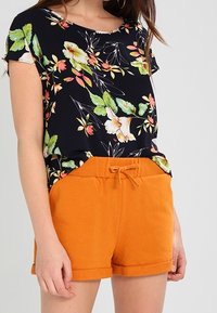 Hedvábný vršek s květinovým vzorem v námořnické modři se shorty v oranžové barvě, které mají elastický pas a šňůrku. Neformální outfit.