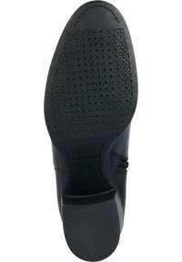 Zapato de cuero negro con una suela de goma texturizada que presenta pequeñas perforaciones circulares para la transpirabilidad, emblema de marca en el lado.