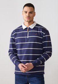 Navy blue long-sleeve polo with white stripes, zip collar, and a small logo on the chest. Made from a textured fabric.