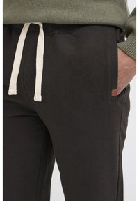 Zwarte katoenen joggers met een crèmekleurige trekkoord taille, zijzakken en een klein bruin logo-opdruk op de voorkant.