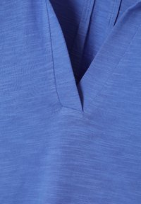 Maglietta blu a scollo a V realizzata in tessuto testurizzato, con un delicato motivo mélange e finiture pulite sul collo e sull'orlo.
