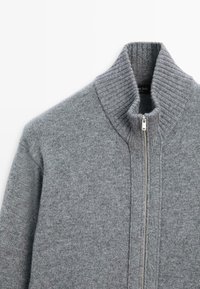 Maglione grigio a maglia con colletto alto, chiusura con zip completa e texture a coste lungo il colletto e i lati. Finitura liscia con dettagli sottili.