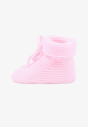 Miękki różowy dziergany bucik dla niemowląt z podwijanym mankietem i małą kokardką zawiązaną przy kostce, przedstawiony na białym tle.