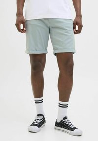 Ljusgröna bomullsshorts med uppvikta fållar, i kombination med svarta sneakers och vita strumpor med svarta ränder.