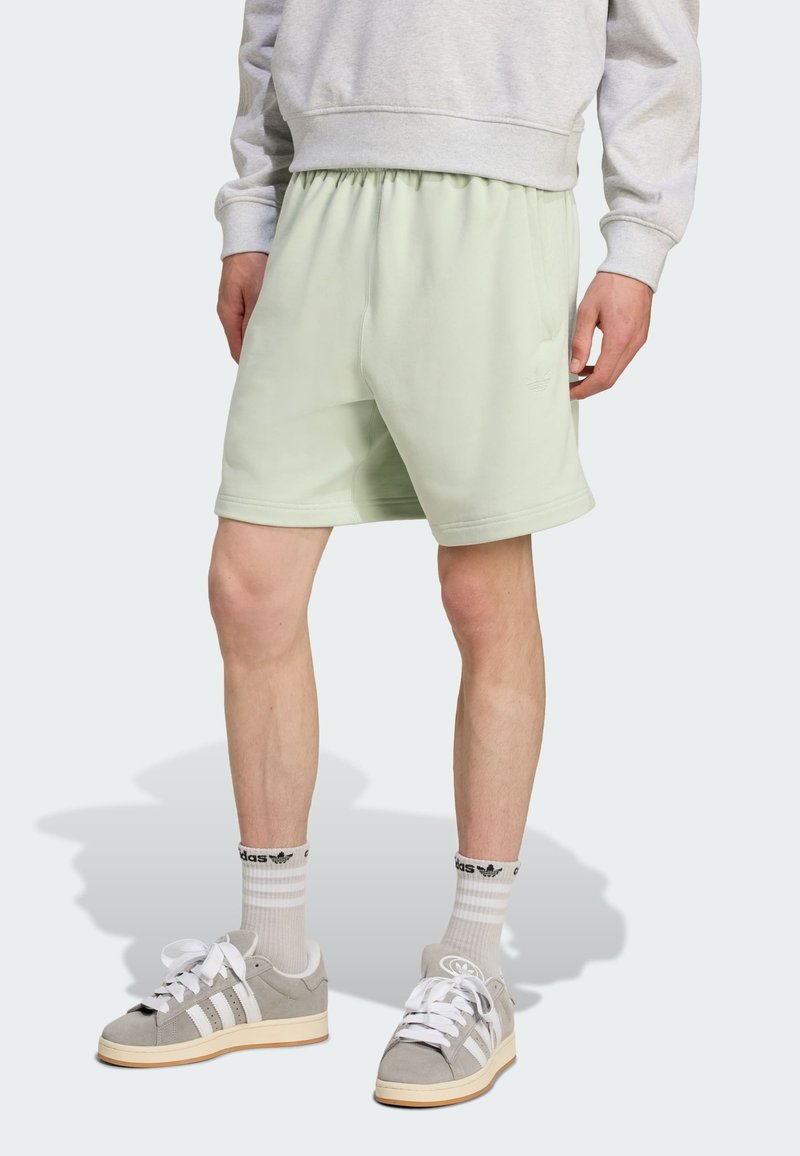 Heledad rohelised puuvillased lühikesed püksid elastse vöökoha, küljetaskute ja väikese logoga. Kandmisel hallid nahast tossud ja valged sokid.