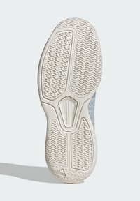 Vit gummi sula på en Adidas-sko med texturerat zigzag-däckmönster och Adidas-logotyp nära hälen på en ljusgrå bakgrund.