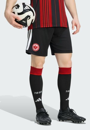 Person i sort og rød fodbolduniform holder en sort og hvid fodbold med sorte knopper og sorte sokker markeret med 1899.