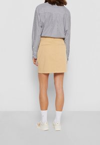 Beige Baumwollrock mit schmaler Passform, zwei Gesäßtaschen und geradem Saum, kombiniert mit einem gestreiften Langarmshirt und weißen Socken.