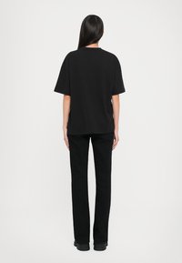 T-shirt nera oversize con maniche corte, in cotone, scollatura rotonda, abbinata a pantaloni neri dritti e calzature scure.