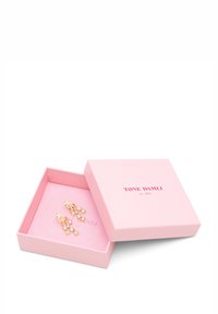 Pendientes en tono dorado con cristales brillantes, exhibidos en una caja de joyería rosa con un inserto rosa suave, que presenta el logotipo de la marca.