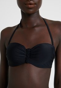 Zwart bandeau bikini-top met gevlochten middenstuk, verstelbare halterbandjes en een gladde stoftextuur.