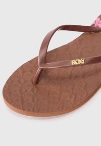 Sandale tongs marron avec une semelle en caoutchouc texturé présentant des motifs circulaires, et des brides marron avec un détail doré "ROXY".