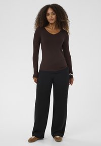 Brun V-hals bluse med lange ærmer kombineret med sorte bukser med vide ben. Blødt stof, tætsiddende silhuet og enkel design. Afslappet fodtøj fuldender looket.