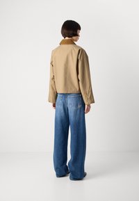 Khaki geknipt jasje met een bruine corduroy kraag, gecombineerd met wijde blauwe denim jeans. Gestructureerde stof, relaxed fit, functionele knopen.