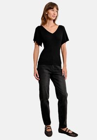 Top corto a maniche corte nero a coste con scollatura a V, abbinato a jeans neri dritti e ballerine in rete nere. Design semplice, stile aderente.