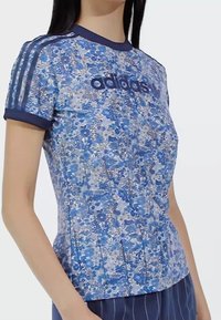 Modra športna majica s cvetličnim vzorcem in kratkimi rokavi, mornarsko modri detajli ter logotipom "adidas" spredaj. Narejena iz lahkega materiala.
