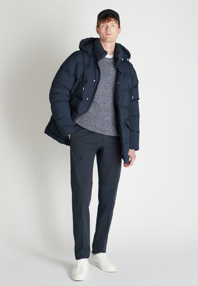 Giacca puffer navy con cappuccio, maglione grigio a trama, pantaloni scuri e sneakers bianche. Presenta una cerniera e dettagli in metallo argento.
