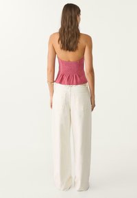 Top sans bretelles rose pâle avec une texture froncée au niveau du corsage et un ourlet en peplum évasé ; associé à un pantalon large léger de couleur claire.