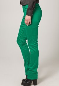 Groene skinny jeans met een gladde textuur, met een hoge taille, zijzakken en decoratieve hardware op de heup. Gecombineerd met zwarte plateauboots.